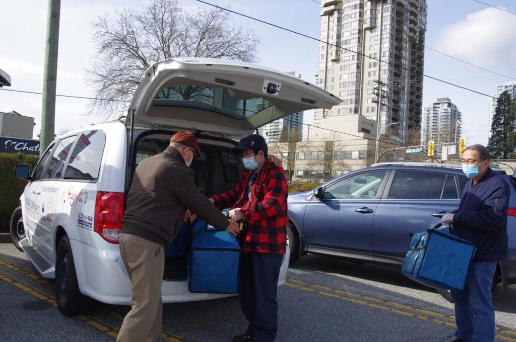 隣組からお弁当を待ち合わせ場所まで運び、利用者宅まで届けるボランティアに引き継ぐ　©The Vancouver Shinpo