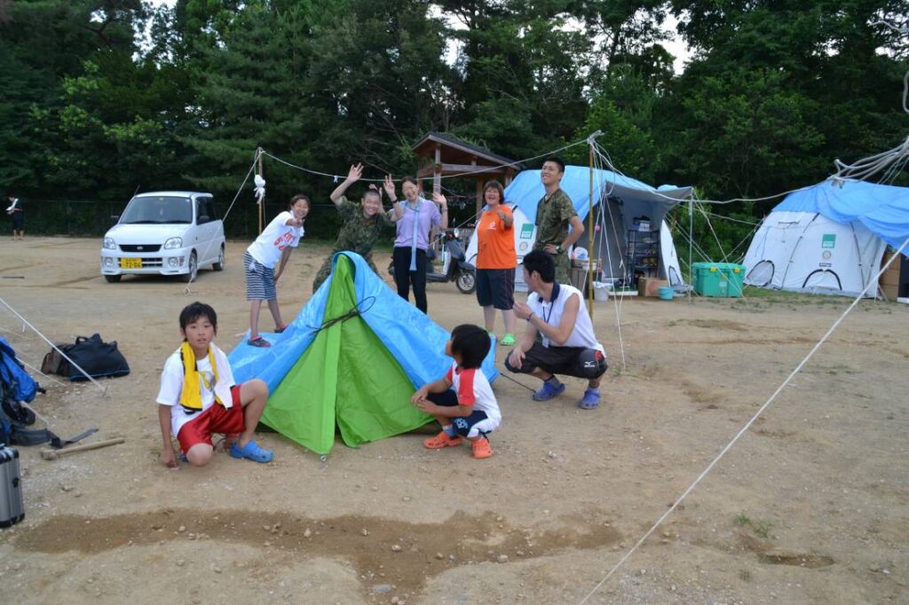 リンダ・オオハマ氏（後方中央）テントキャンプで被災者と。2011年、宮城県女川町。Photo courtesy of Linda Ohama
