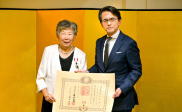 叙勲受章ルース・ミドリ・コールズ氏に勲記と勲章を伝達 勲章を胸に、勲記を手にするコールズ氏(左)、丸山総領事と。2022年12月27日、在バンクーバー日本国総領事公邸。Photo by ©Koichi Saito