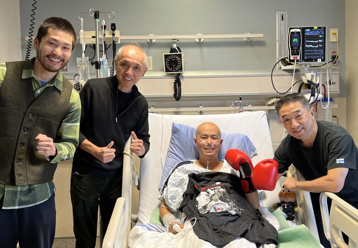 病室に移っての治療を続ける米澤幸也さんを訪問。左から、丸岡裕典さん、サミー高橋さん、ハリーさん、吉川英治さん。写真提供：サミー高橋さん