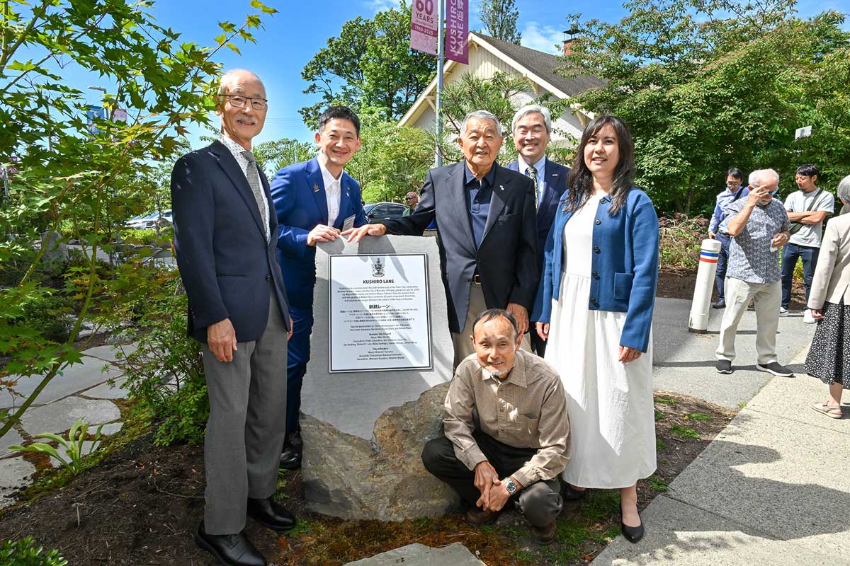 左から、ケン・シノザキさん、釧路市鶴間秀典市長、ヘンリー・ワカバヤシさん、ハーブ小野さん、日系センター事務局長ケーラ・ゴシンモンさん、前列にニック・スエヨシさん。「釧路レーン」を説明するプレートを囲んで。2025年7月13日、バーナビー市。撮影　斉藤光一