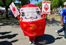 第50回パウエル祭、今年もイベント満載 プログラムの詳細発表 パウエル祭のキャラクター・ダルマが会場を歩き、ボードを手に来場者との記念撮影に応じて会場を盛り上げた。2025年8月2日、バンクーバー市。Photo by Koichi Saito/Japan Canada Today