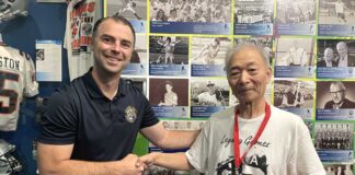 「朝日軍」初代団長の孫・松宮哲さん、BCスポーツ殿堂博物館を訪問 BCスポーツ殿堂博物館で、殿堂担当者のベックさん(左)と記念メダルを持つ松宮さん(右)。長年の交流を経て、歴史的な節目の日に訪問が実現した。2025年9月18日、バンクーバー市。撮影 田上麻里亜/日加トゥデイ