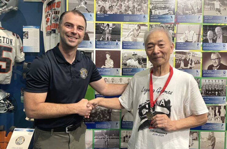 「朝日軍」初代団長の孫・松宮哲さん、BCスポーツ殿堂博物館を訪問 BCスポーツ殿堂博物館で、殿堂担当者のベックさん(左)と記念メダルを持つ松宮さん(右)。長年の交流を経て、歴史的な節目の日に訪問が実現した。2025年9月18日、バンクーバー市。撮影 田上麻里亜/日加トゥデイ