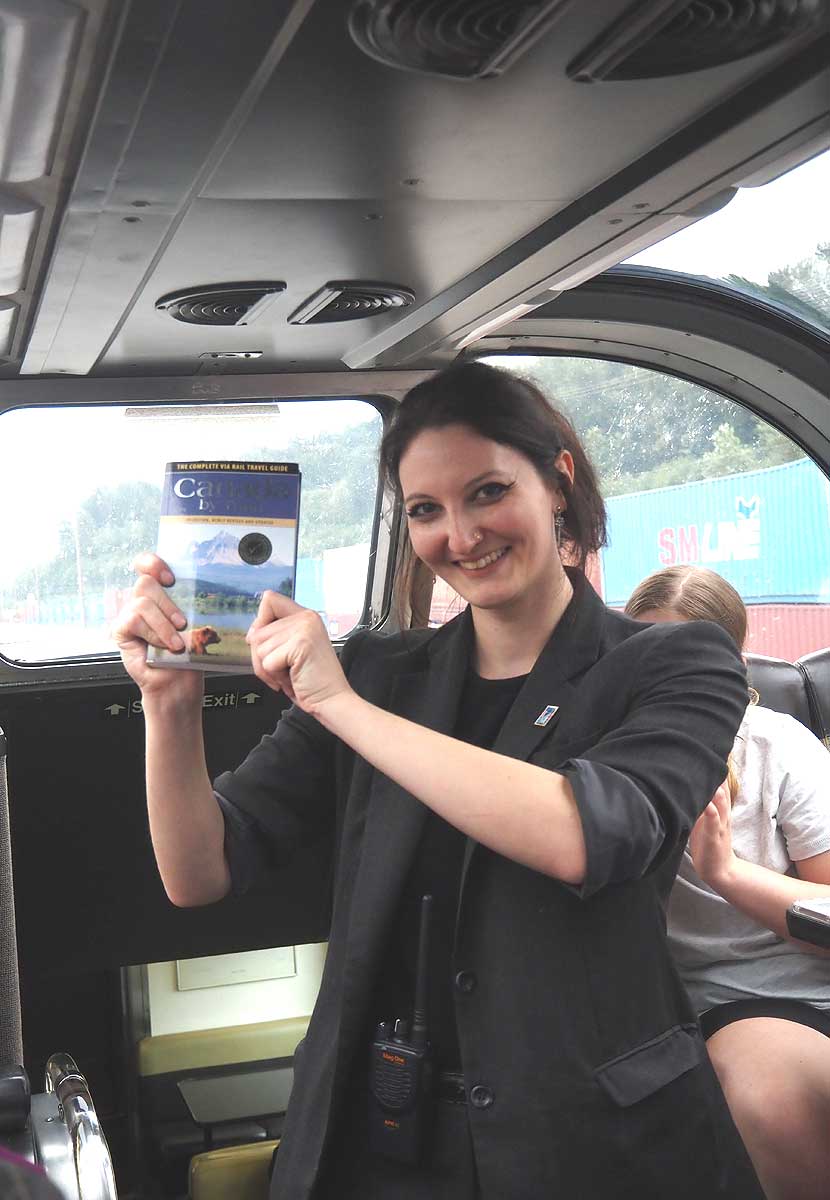 VIA鉄道カナダの列車「カナディアン」に連結されたスカイラインドームカーで、書籍を示す客室乗務員のエミリー・ファラージさん(ブリティッシュ・コロンビア州で大塚圭一郎撮影)
