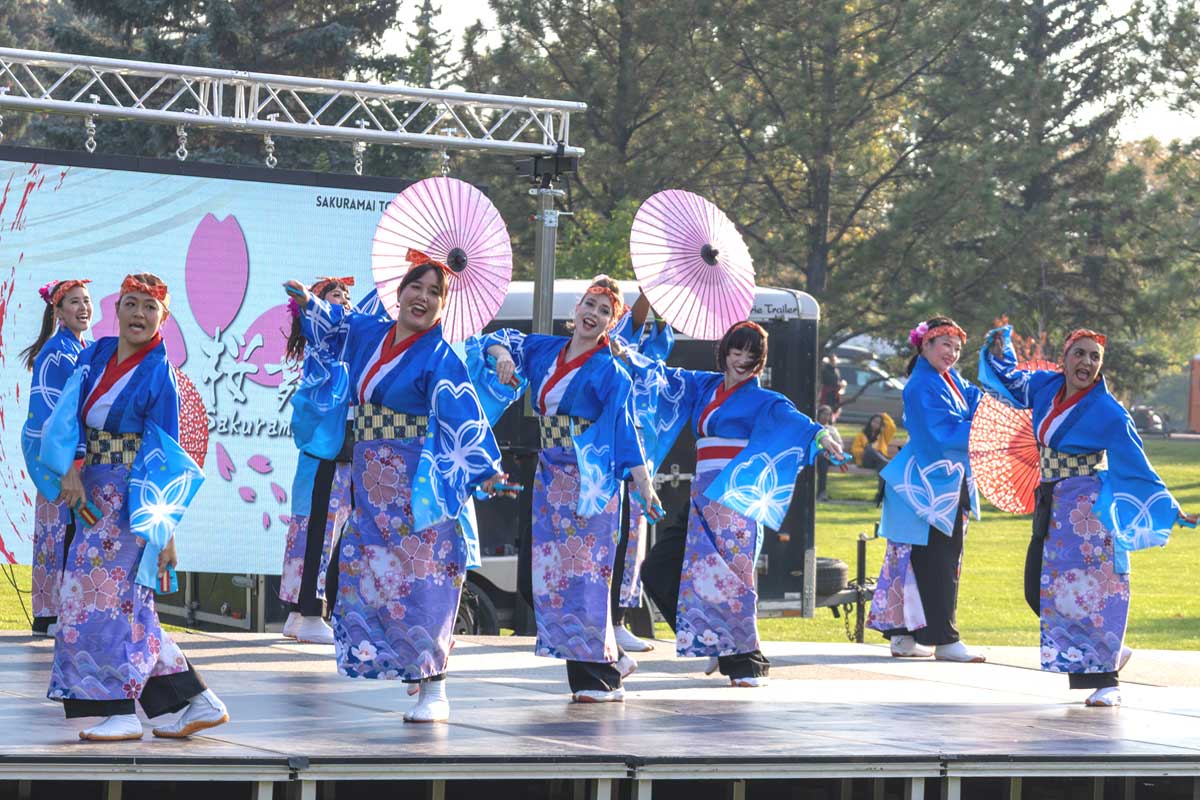 桜の模様が鮮やかな青い衣装をまとい、和傘を手に舞う「桜舞トロント(Sakuramai Toronto)」の踊り子たち。トロントを拠点に、カナダ各地でよさこいの魅力を伝えている。2025年9月27日、アルバータ州レスブリッジ市。提供: KOKUYOSA Project Committee