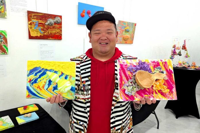 1_Arapon_2025-9 作品を持つあらぽんさん。展示会場で。2025年9月1日、バンクーバー市。撮影 三島直美/日加トゥデイ