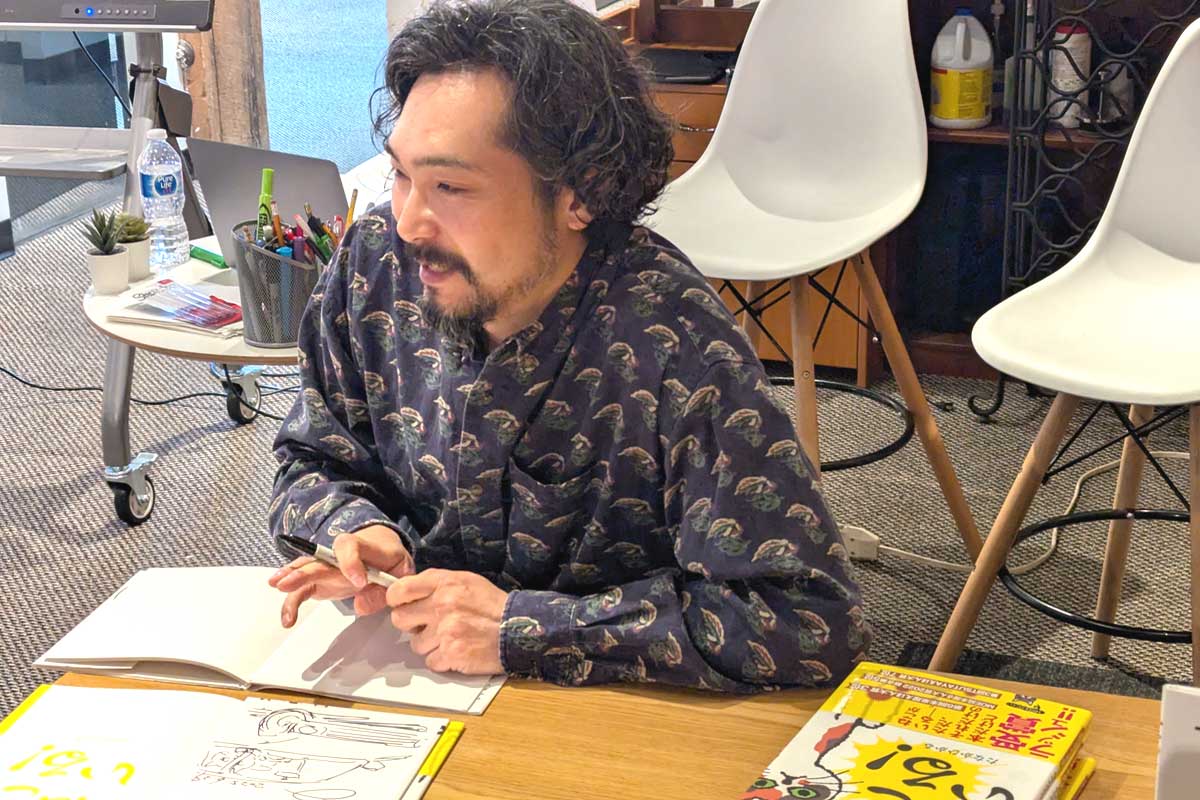 イベント終了後に参加者の求めに応じて記念撮影や絵本に自筆の絵とサインをする田中さん。2025年6月29日、バンクーバー市。撮影　三島直美／日加トゥデイ