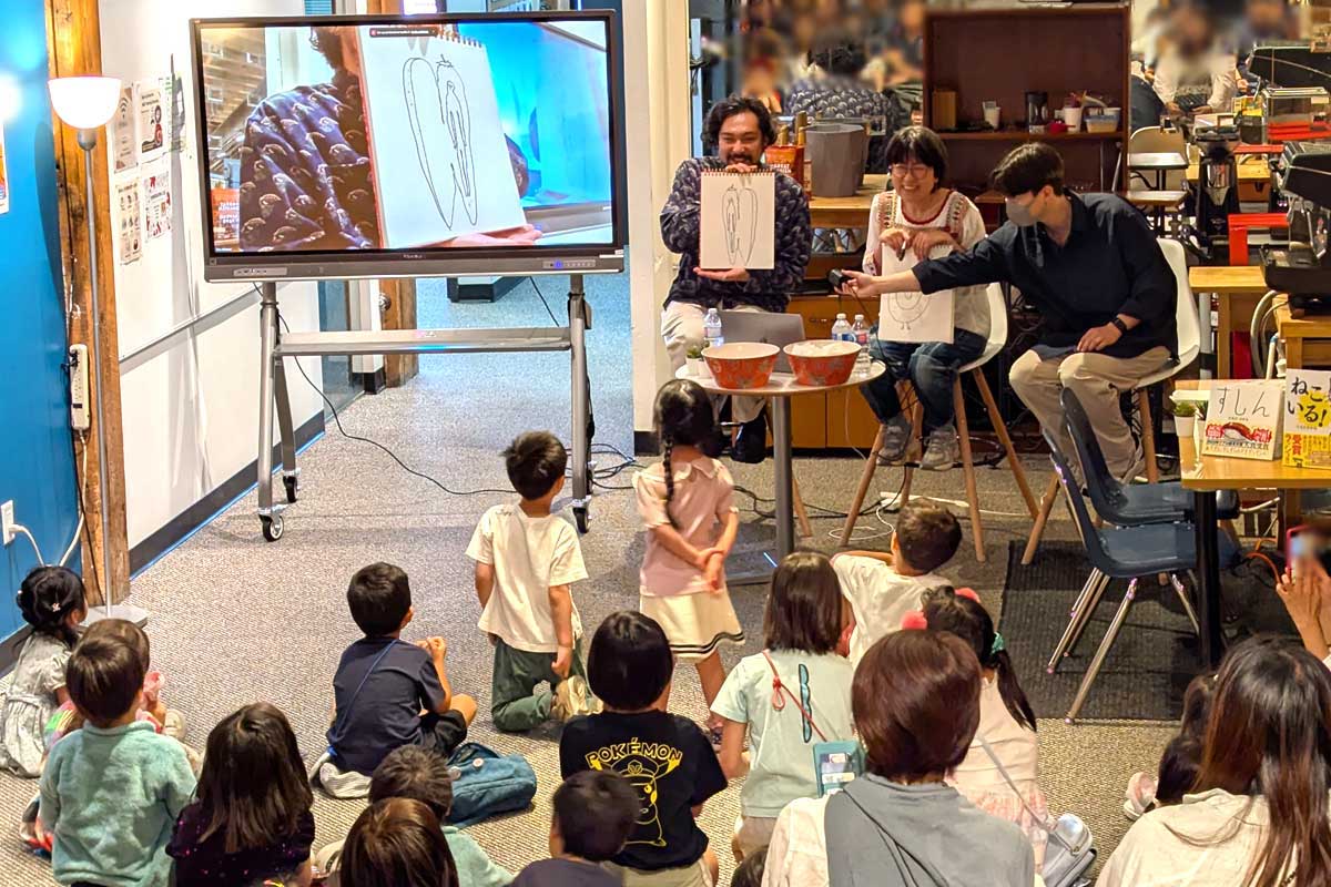 造語からインスピレーションを受けて描いた自身の絵を子どもたちに見せる田中光さん（左）、一緒にイベントを盛り上げた光浦靖子さん（中央）、カメラを操作するウィトレッド太朗さん（右）。2025年6月29日、バンクーバー市。撮影　三島直美／日加トゥデイ