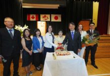 55年の世代を超えて グラッドストーン日本語学園祝賀同窓会 創立55周年を祝うケーキ。卒業生や髙橋良明総領事などに囲まれ、笑顔を見せる村上陽子学園長(右から4番目)。2026年5月30日、日系文化センターホール。写真提供 グラッドストーン日本語学園