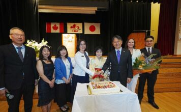 55年の世代を超えて グラッドストーン日本語学園祝賀同窓会 創立55周年を祝うケーキ。卒業生や髙橋良明総領事などに囲まれ、笑顔を見せる村上陽子学園長(右から4番目)。2026年5月30日、日系文化センターホール。写真提供 グラッドストーン日本語学園