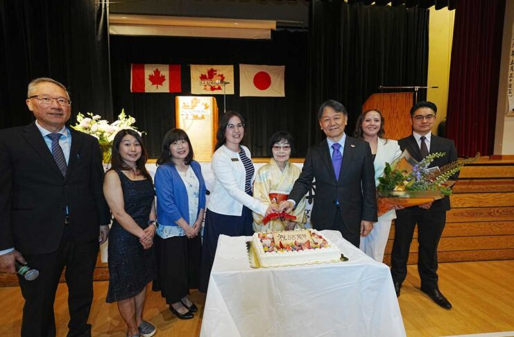 55年の世代を超えて グラッドストーン日本語学園祝賀同窓会 創立55周年を祝うケーキ。卒業生や髙橋良明総領事などに囲まれ、笑顔を見せる村上陽子学園長(右から4番目)。2026年5月30日、日系文化センターホール。写真提供 グラッドストーン日本語学園