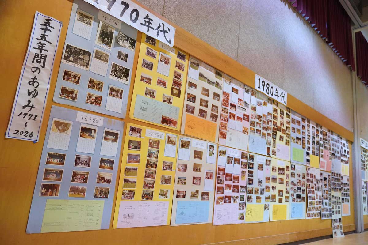 会場の壁に展示された「55年間のあゆみ　1971〜2026」。1970年代から年代別に並べられた写真や資料の前で、来場者たちが思い思いに言葉を交わした。2026年5月30日、日系文化センターホール。写真提供　グラッドストーン日本語学園