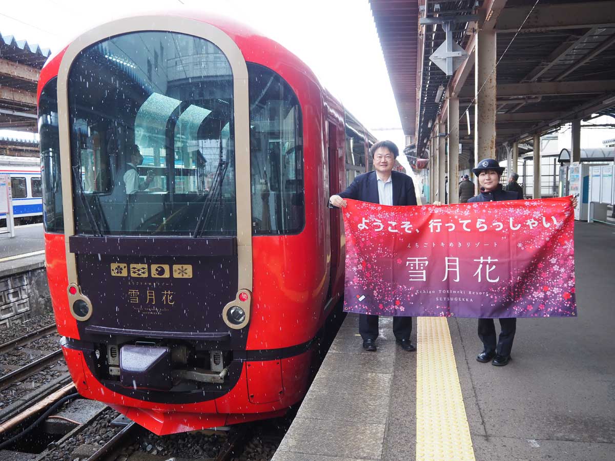 「えちごトキめきリゾート雪月花」の前で横断幕を掲げる客室乗務員(右)と筆者